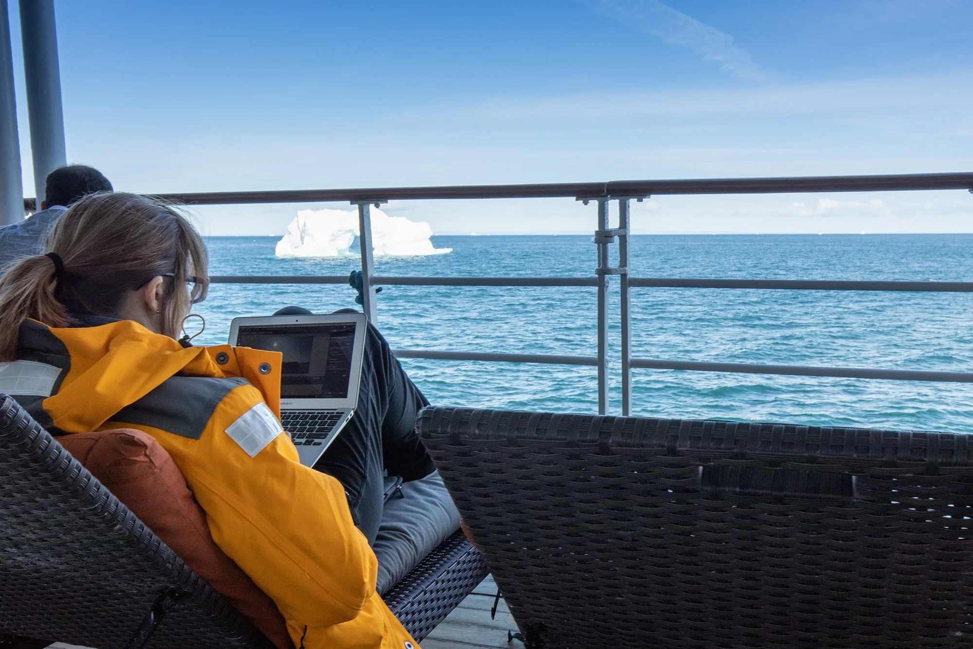 Woman using her laptop with an iceberg in the distance while in Antarctica