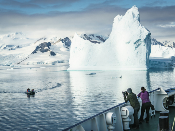 Tourists taking photos of an iceberg from a vessel in Antarctica